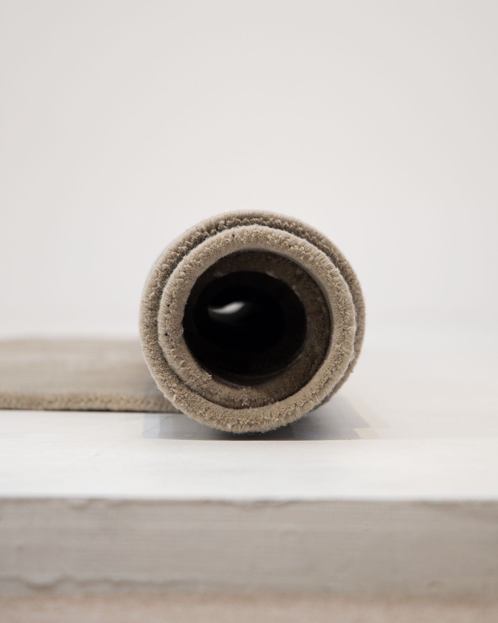 A rolled-up Natural White Color Handmade Area Rug by RAMSHA HOME (HTWV-137, 200x300 cm) sits on a white surface, viewed head-on to reveal the circular layers of fabric.