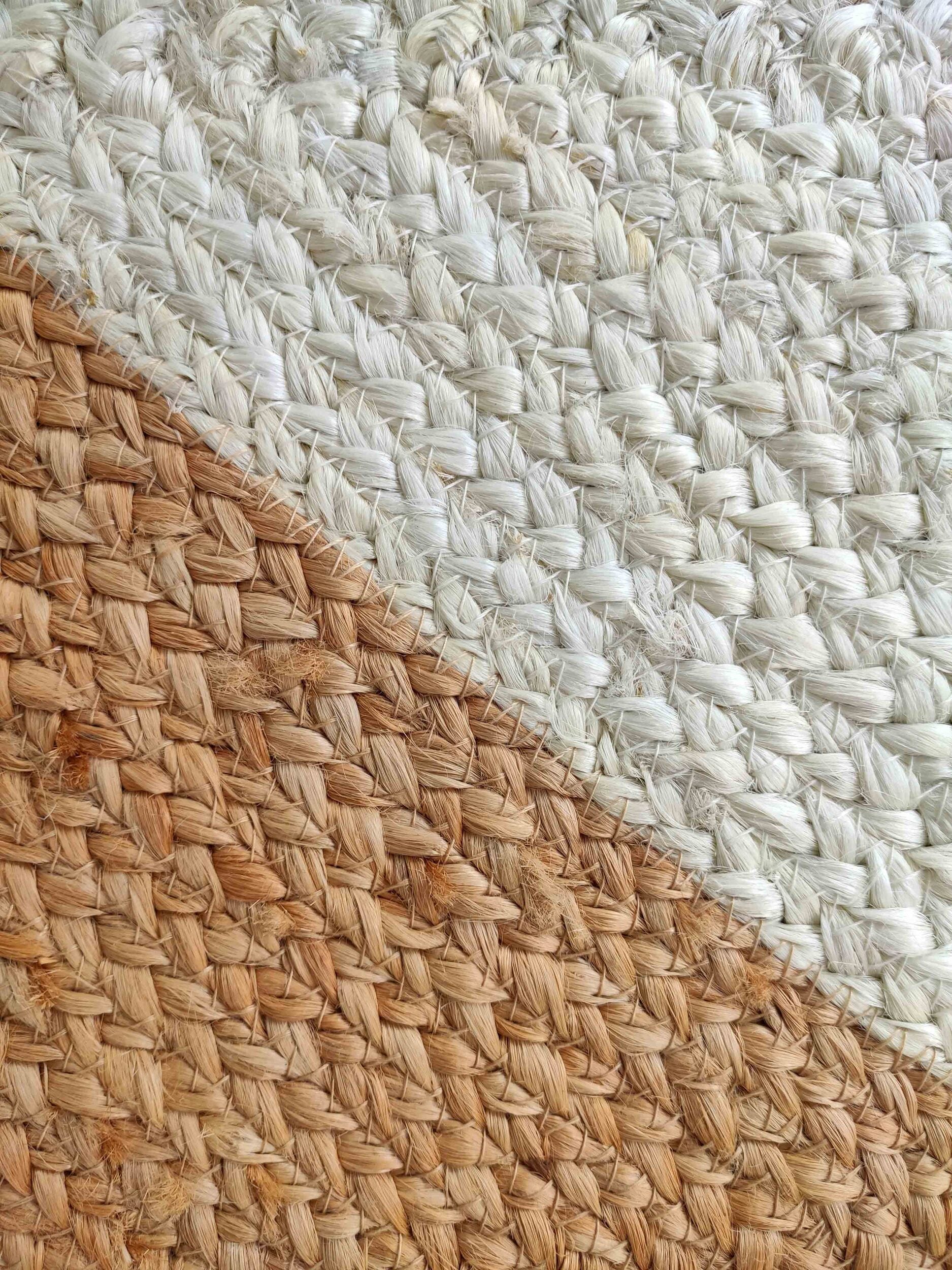 Close-up of the RAMSHA HOME Beautiful Handmade Natural & Bleach Color Jute Braided Rug with Tassel (BR 031), showing a diagonal divide between light and natural jute, emphasizing its woven texture and pattern.