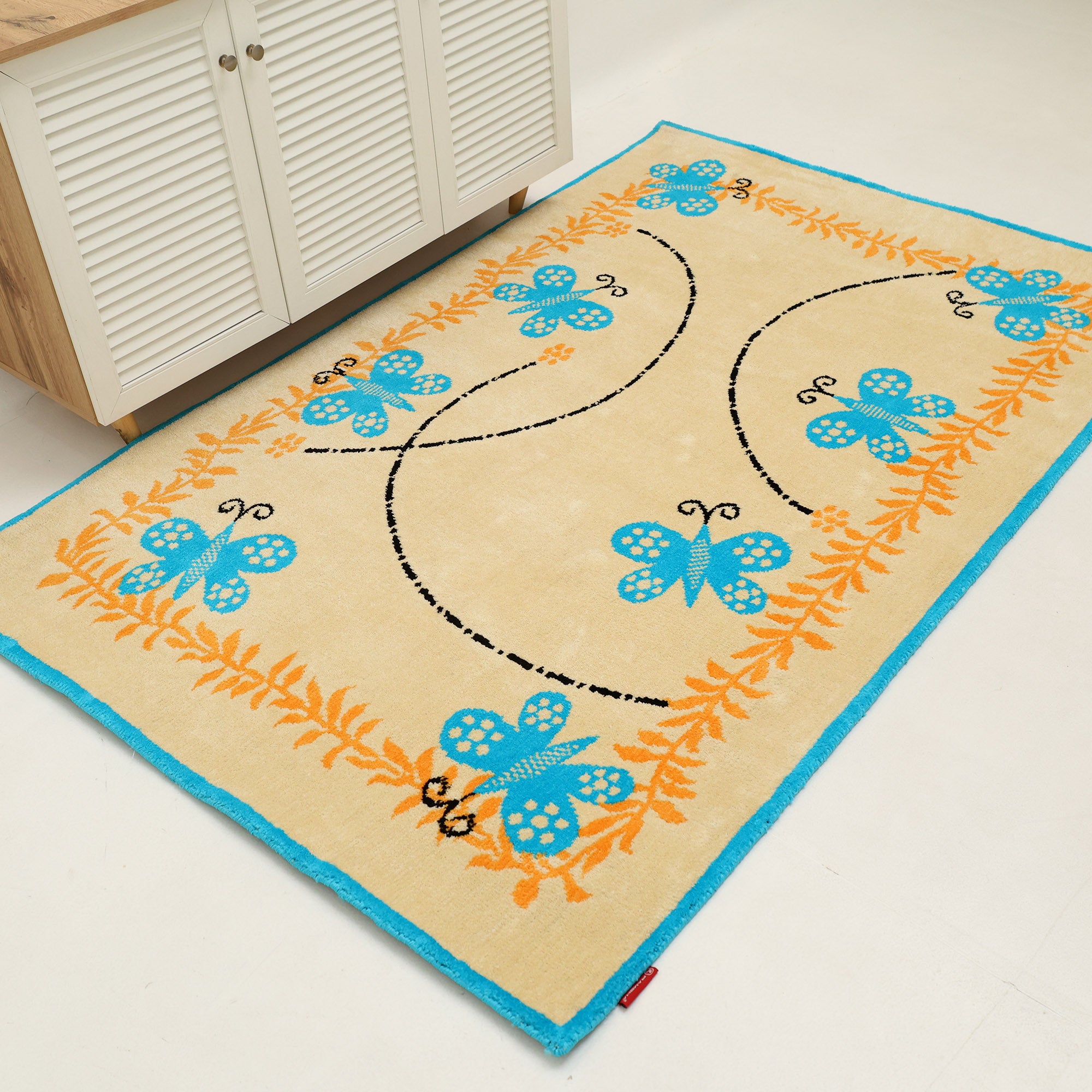 The RAMSHA HOME Kids Rug Soft Multi Color Nursery Rug 120x180 cm – KD 022 features blue butterflies, an orange floral border, and black dotted lines—ideal for brightening up any nursery or kids’ space.
