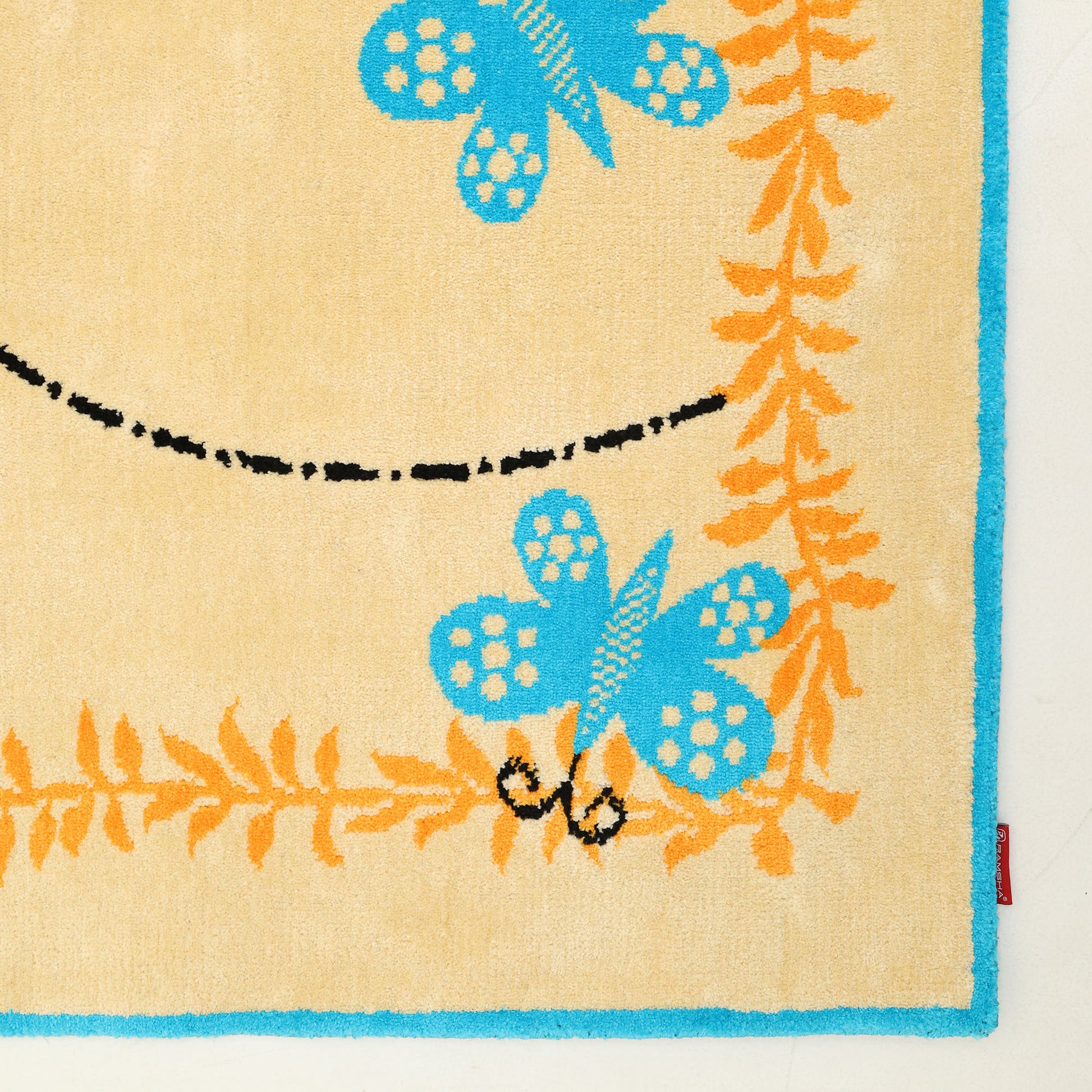 The RAMSHA HOME Kids Rug Soft Multi Color Nursery Rug 120x180 cm (KD 022) features a beige base, blue border, orange fern patterns, and blue butterflies with a dashed flight path—perfect for any nursery or playroom.