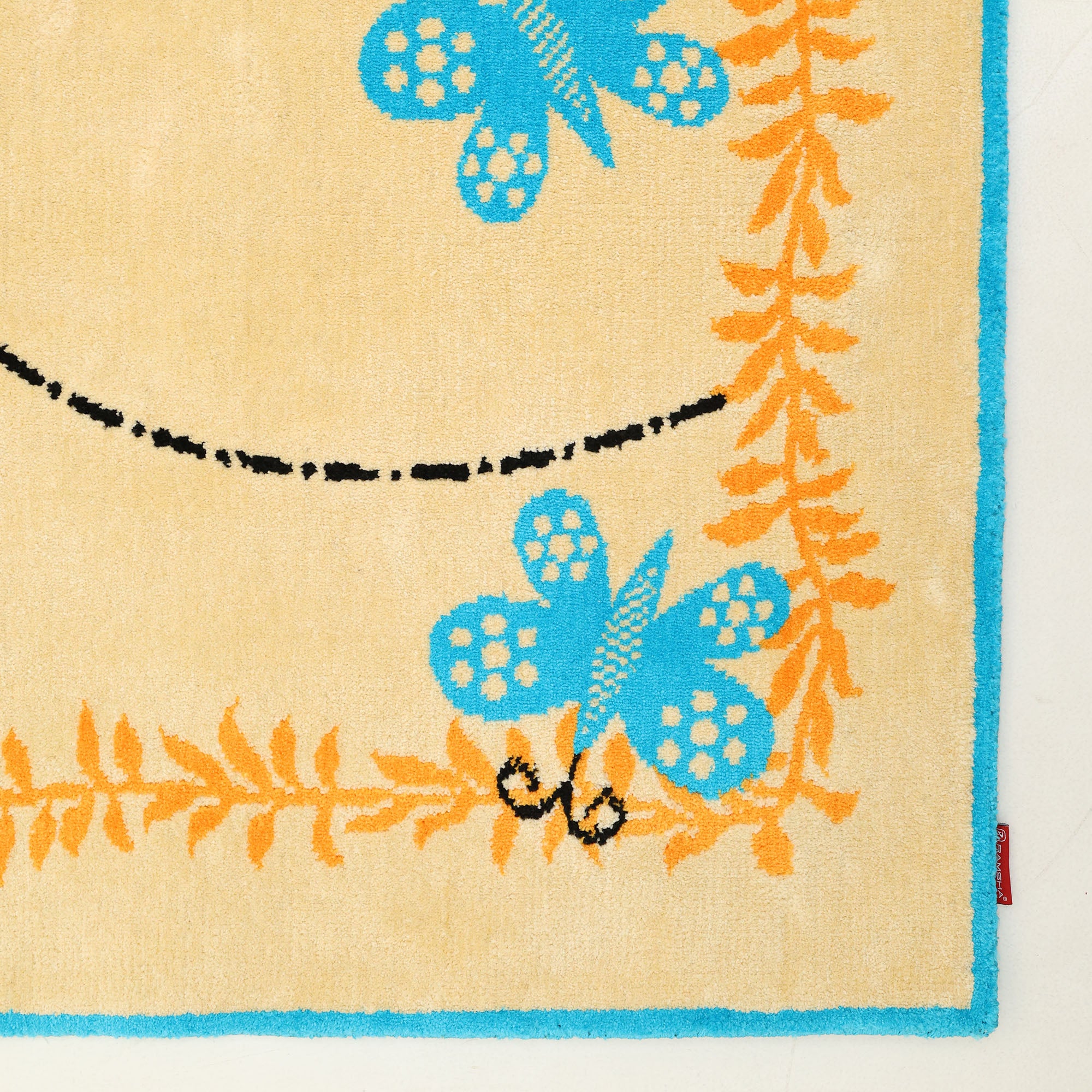 The RAMSHA HOME Kids Rug Soft Multi Color Nursery Rug 120x180 cm (KD 022) features a beige base, blue border, orange fern patterns, and blue butterflies with a dashed flight path—perfect for any nursery or playroom.