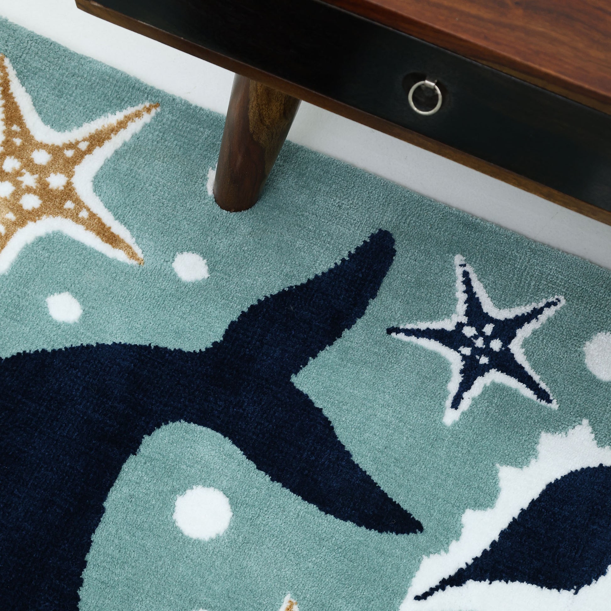 A close-up of the RAMSHA HOME Kids Rug Soft Whale Character Rug 120x180 cm – KD 017, with a marine theme featuring a whale tail, starfish, and bubbles beside a wooden table—ideal for nursery or kids' bedrooms.