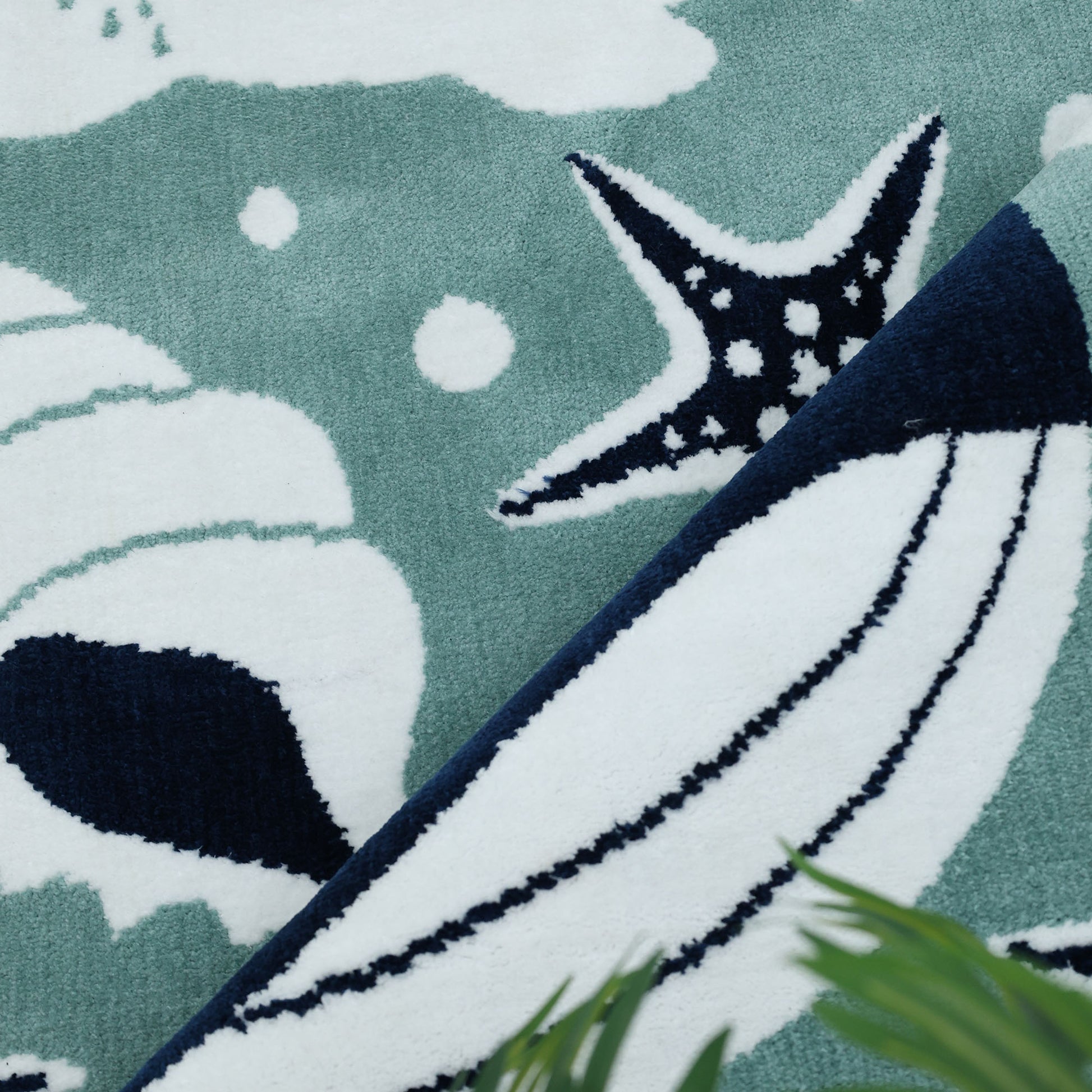 Close-up of the RAMSHA HOME Kids Rug Soft Whale Character Rug (120x180 cm – KD 017), showing playful starfish, waves, and bubbles in teal, white, and navy blue, with a green leaf partially visible in the corner.