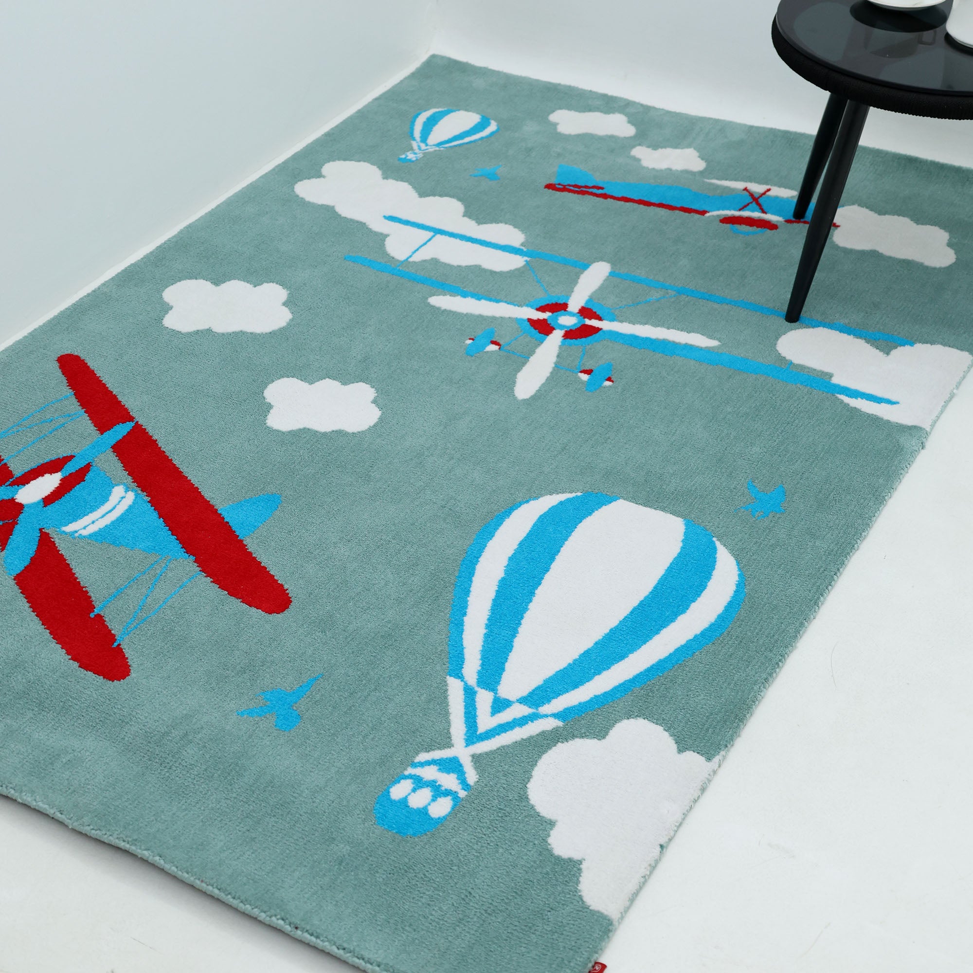 The RAMSHA HOME Kids Rug Soft Multi Color Nursery Rug 120x180 cm – KD 020 adds playful charm to a kids’ room with pastel tones and fun motifs—ideal beside a round black side table in a minimalist nursery.