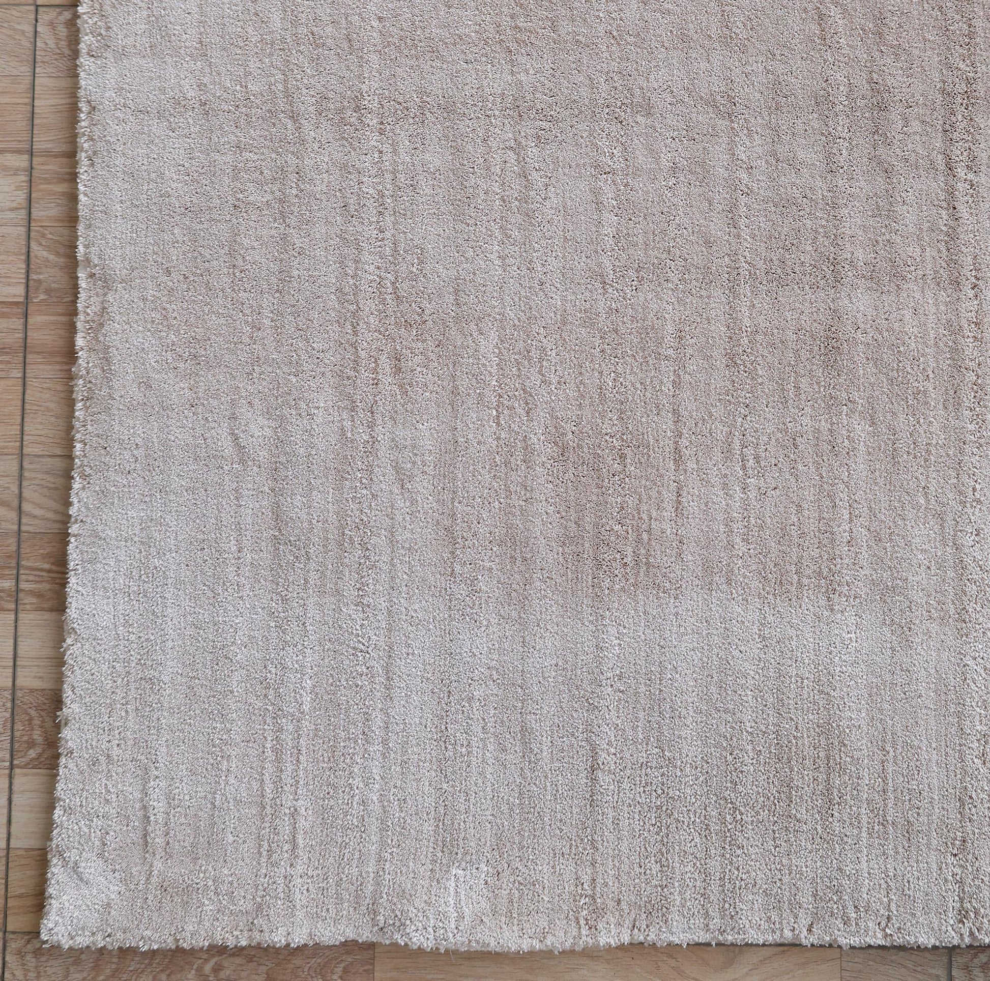 The RAMSHA HOME Handmade Plain beige Area Color Rug (300x400 cm, LKH-047) is shown on a wooden floor, featuring a soft, cream-toned surface with subtle linear details and a slightly uneven edge.