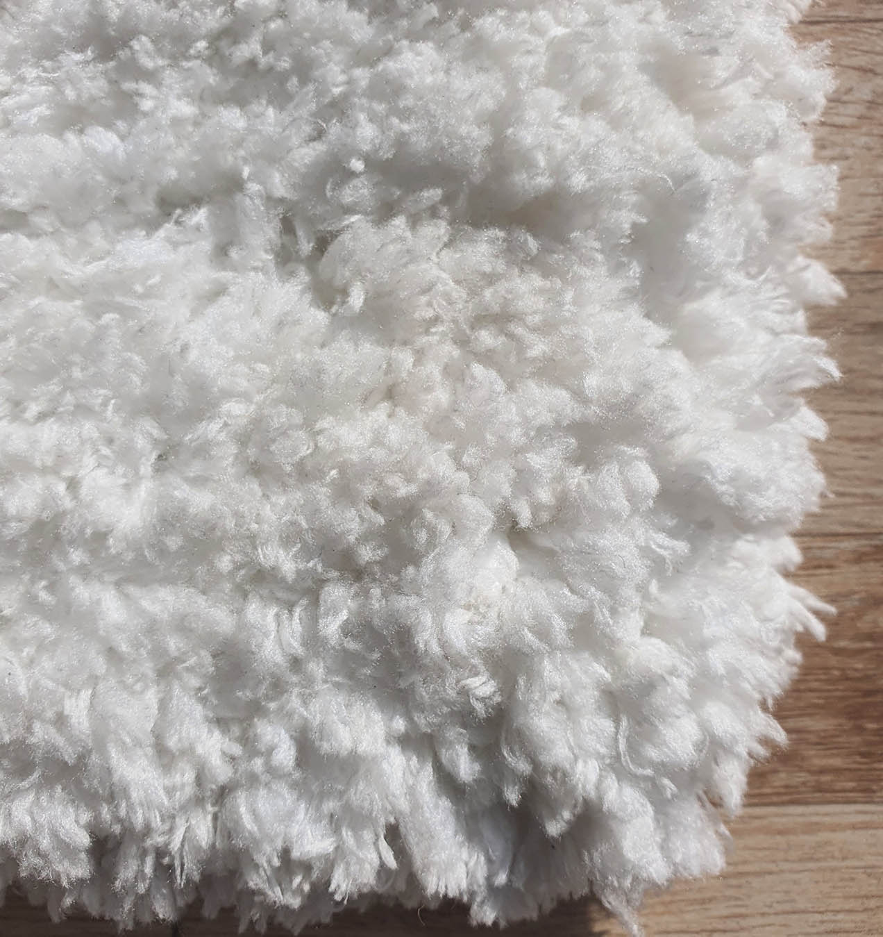 A close-up of the RAMSHA HOME Soft White Rectangle Bedroom Shaggy Rug - SG 06, showcasing its plush ivory pebbled shag texture highlighted in bright natural light on a wooden floor.