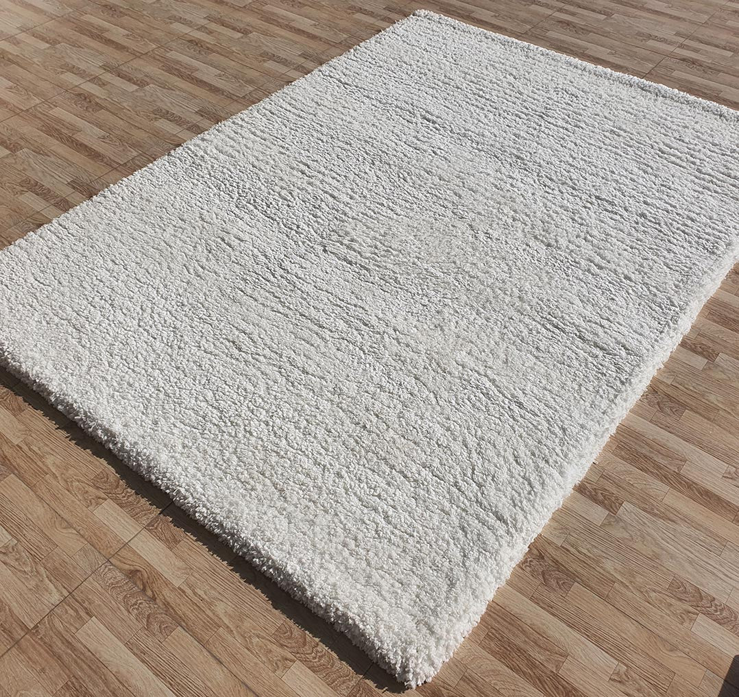 The RAMSHA HOME Soft White Rectangle Bedroom Shaggy Rug - SG 06 features a plush, textured surface and crisp edges, creating a striking contrast against the light wood-patterned floor beneath it.
