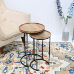 Set of 2 wooden nesting side tables with round solid wood tops and black iron bases placed in front of a couch