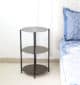 Round wooden side table with black metal base placed beside the bed – modern bedside furniture
