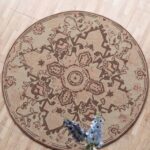 An Artisanal Round Wool Rug with a brown and beige vintage medallion pattern on a light wooden floor.