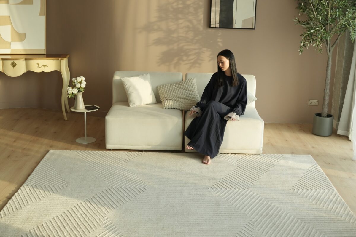 A spacious modern living room featuring a large grey rectangular rugs anchoring a sectional sofa and coffee table.