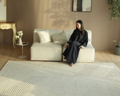 A spacious modern living room featuring a large grey rectangular rugs anchoring a sectional sofa and coffee table.